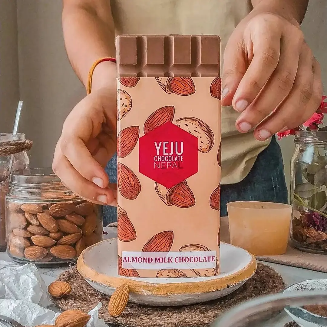 Yeju almond milk chocolate bar, held over a plate of almonds